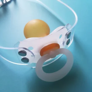 Detail of a white NUK pacifier shield and ring attached to a clear PVC strap.