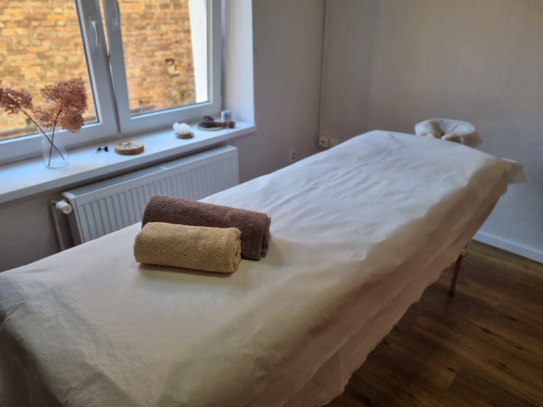 Vlaďka Kouklová – massage table with a white sheet and folded towels beside a window.