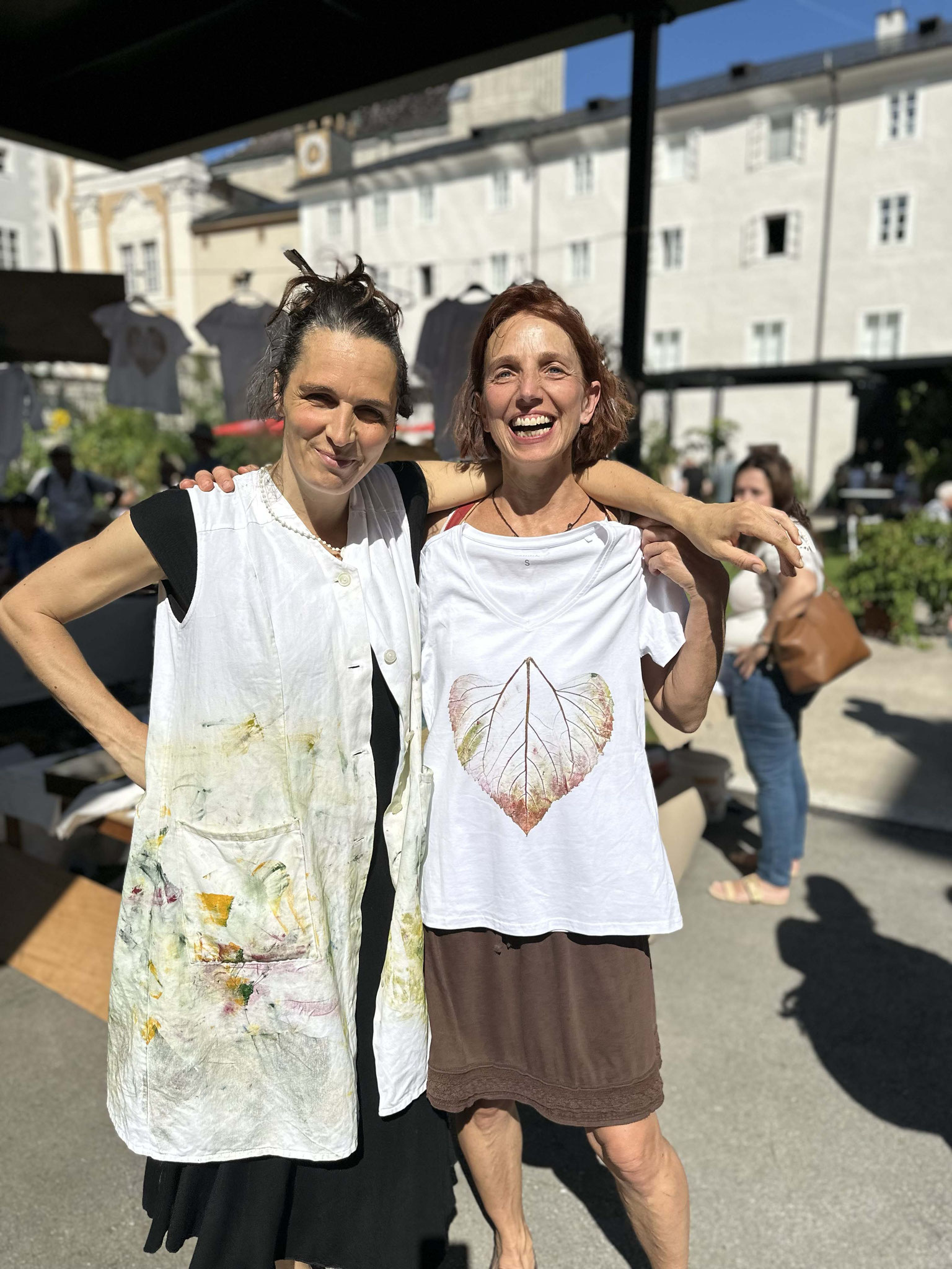 Nature Art Daniela Gruber – two women wearing hand-decorated aprons at an outdoor event.