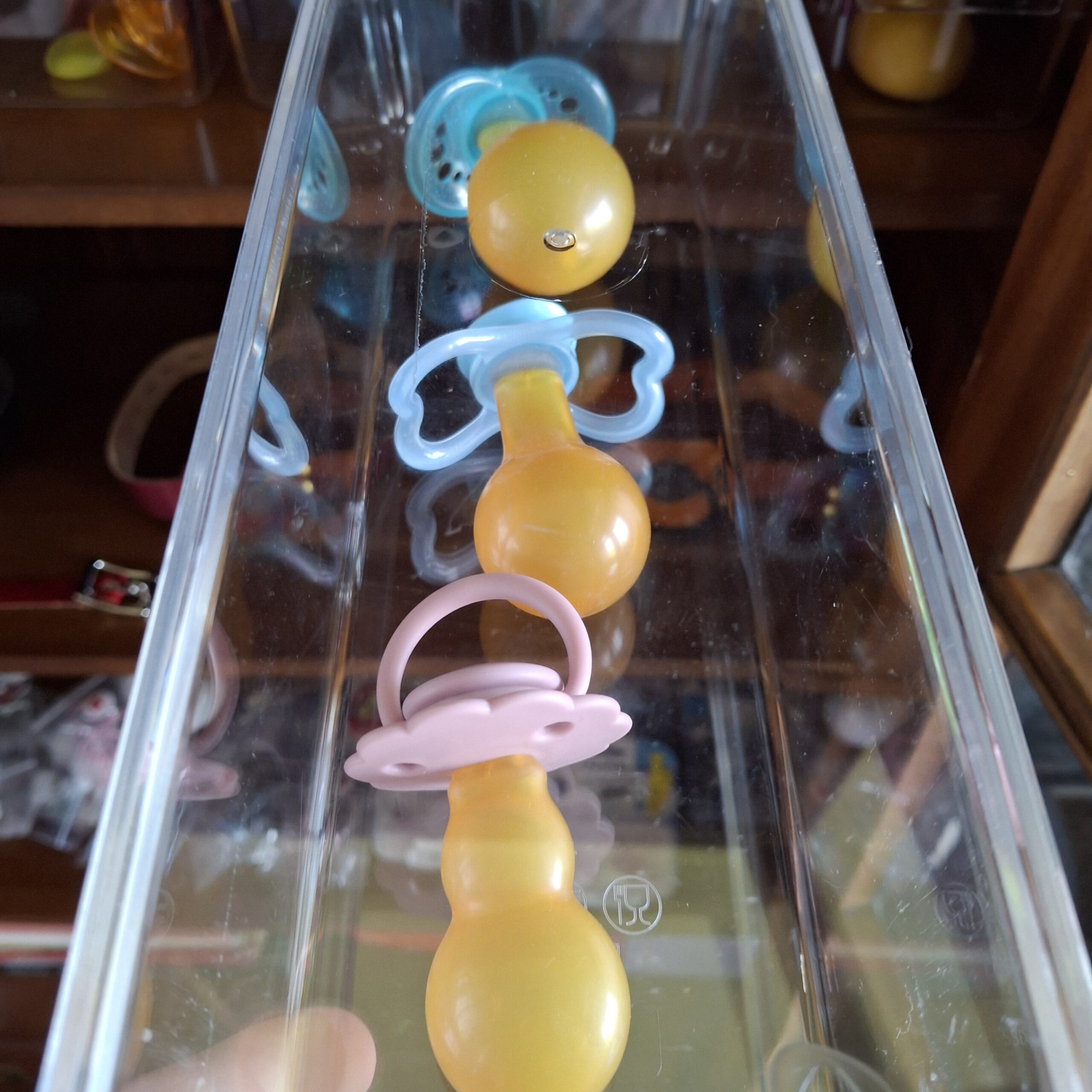 Row of latex pacifiers with different teat shapes in a clear doodoo showroom organiser.