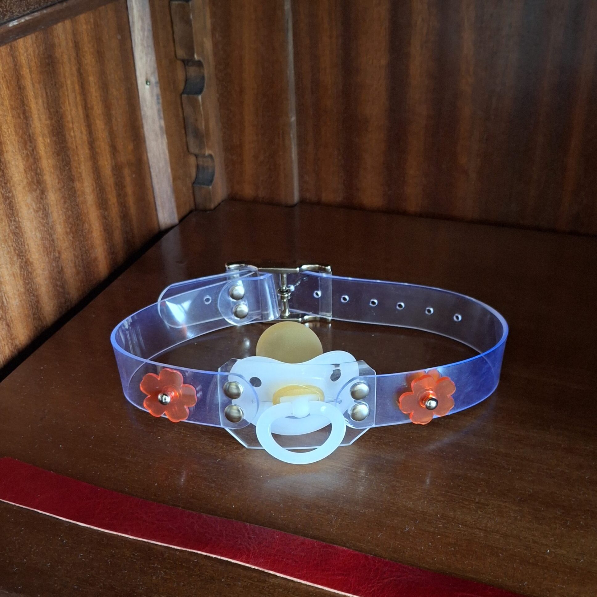 Clear PVC strap with a white pacifier and red decorative fasteners in the doodoo showroom.