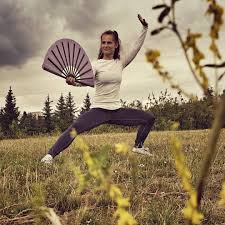 Taiji │ Martina Slabá – woman practising taiji with an open fan in a meadow.