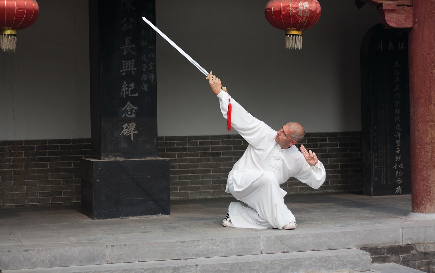 Taiji akademie – person in white clothing practising with a sword in front of a traditional building.